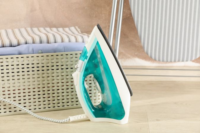 Iron and basket with laundry against brown background, space for text
