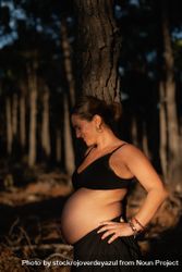 A pregnant woman holds her belly and smiles wearing underwear in the woods 0LddgX