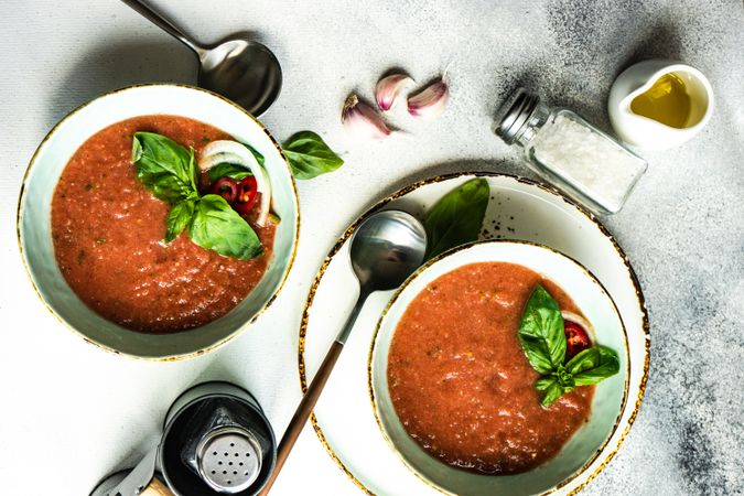 Top view of two bowls of traditional gazpacho soup with olive oil, basil, garlic and pepper