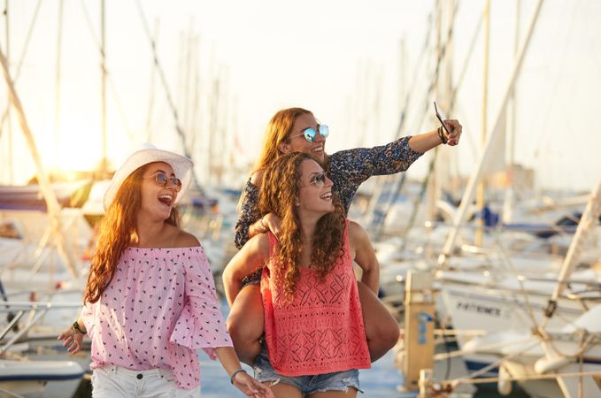 Woman carrying girlfriend on back and taking selfie