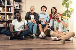 Diverse group of young friends laughing and watching a movie at home, eating popcorn.