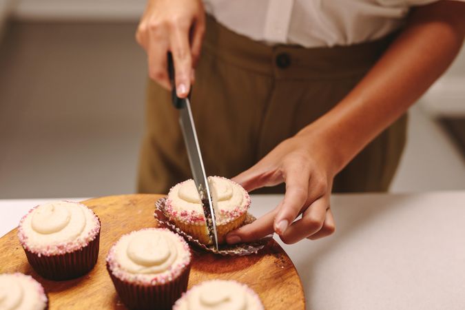 Close up shot of pastry chef slicing cupcake on wooden board with knife