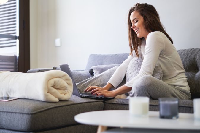 Smiling woman browsing on laptop and sitting on settee