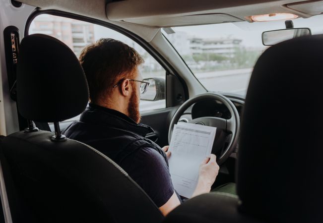 Courier filling papers while preparing for delivery of order to client in car