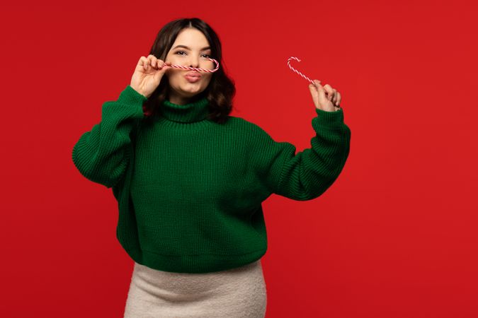 Woman in green sweater playfully holding two candy canes