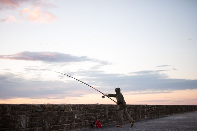 Person holding a fishing rod and standing on the beach during sunset