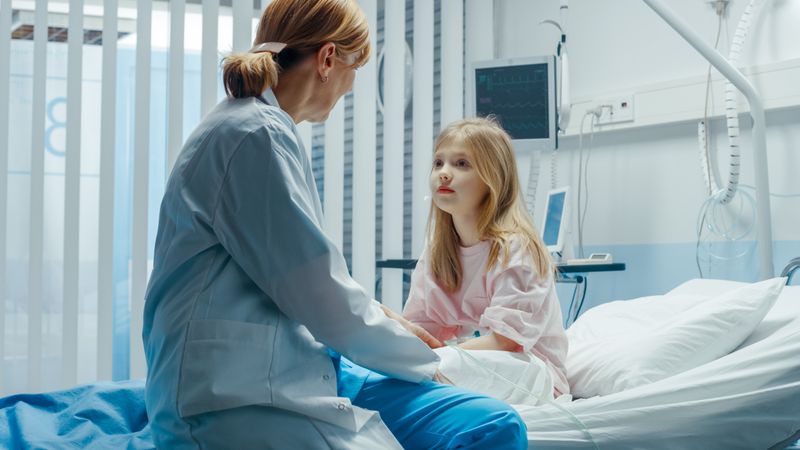 Recovering Little Girl Sits on a Hospital Bed and Talks with Friendly Woman Doctor