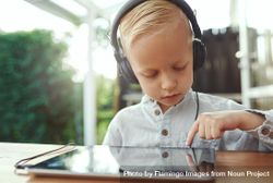 Blond boy using headphones and selecting show or game on digital tablet 4NdWm0