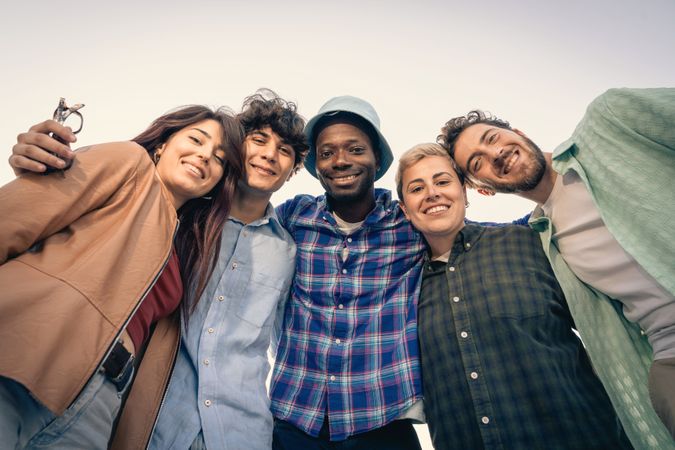 Happy diverse group of young friends hugging and smiling at camera outdoors.