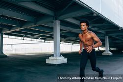 Black athletic male jogging under a bridge 0VxYN4