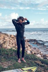 Sporty ethnic male surfer standing near surfboard on rocky seash