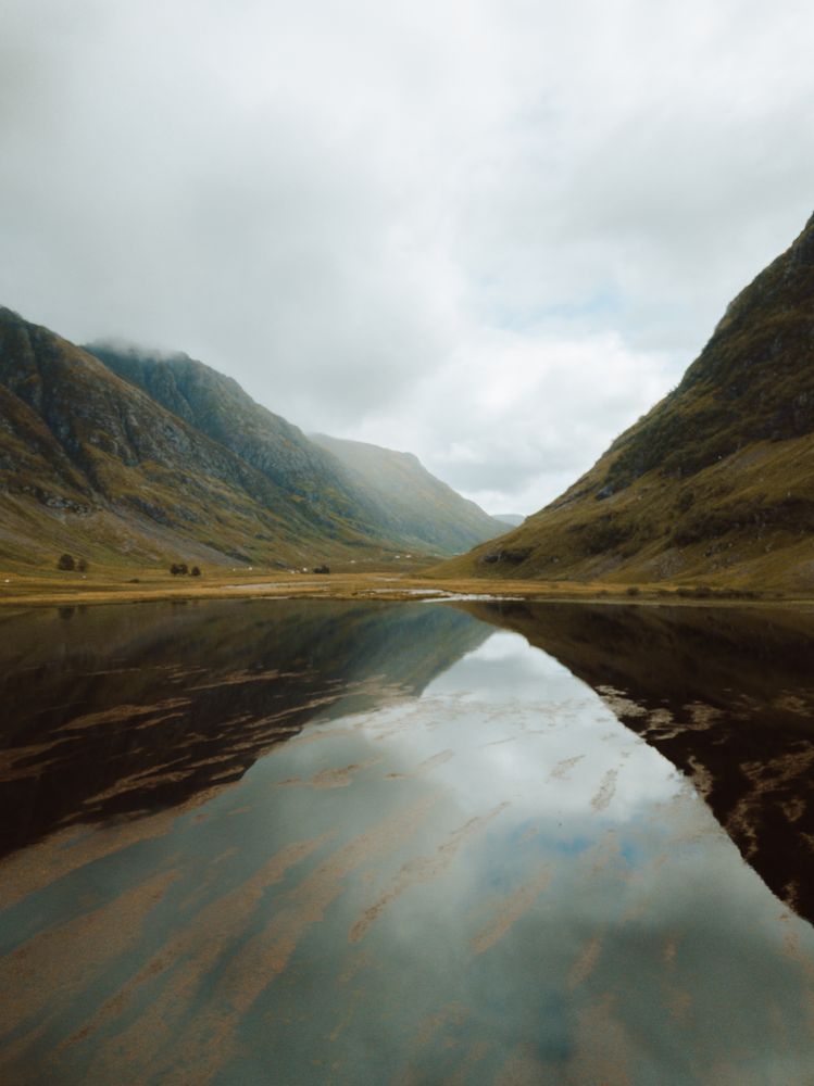 Tranquil lake amidst hills on cloudy day