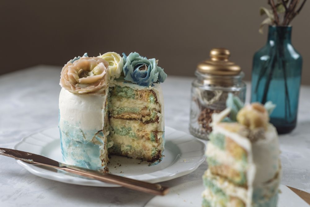 Portion of rainbow cake, filled with chantilly cream, and decorated with buttercream flowers