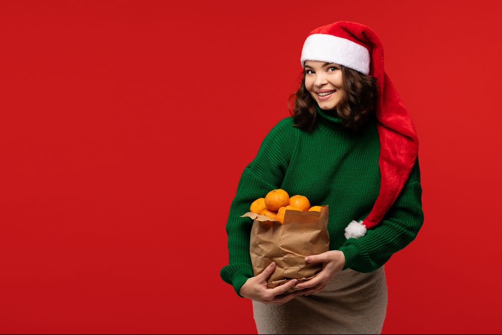 Woman in Santa hat holding bag of fresh tangerines
