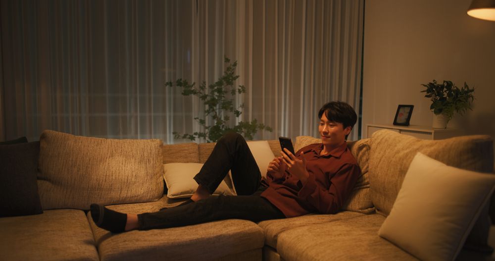 South Korean Young Man Enjoying His Leisure Time while Relaxing and Using a Smartphone