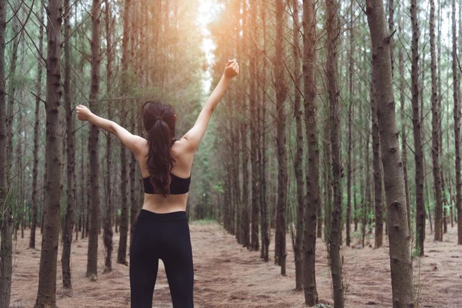 Woman stretching arms up along forest path in forest