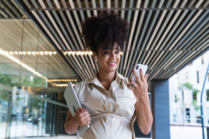 Smiling Black pregnant woman using smartphone and wireless earphones