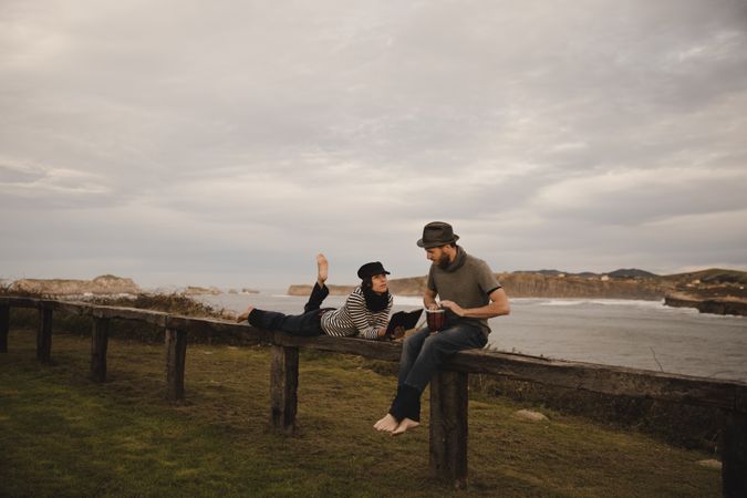 Man plying on drum near woman with notebook on bench on shore