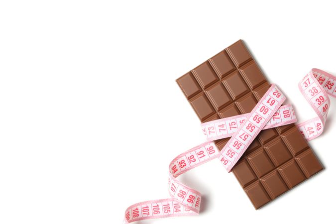 Measuring tape and chocolate bar on light background