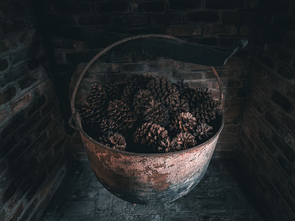 Large pine cones inside cast iron cauldron hanging in fireplace