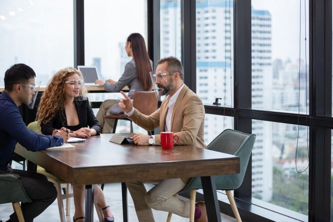 Male manager in face shield discussing work project to colleagues in the office