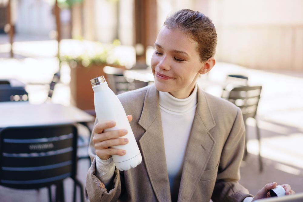A Woman Happily Enjoying Her Colorful Water Bottle While Seated in a Cafeteria Setting