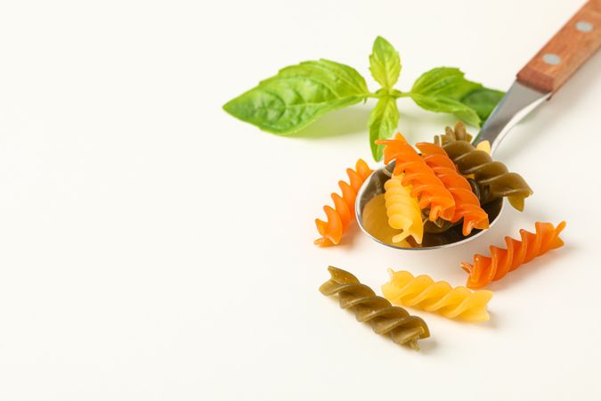 Spoon with color pasta on plain background, space for text and closeup