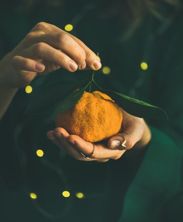 Woman in green holding tangerine, with fairy lights, copy space