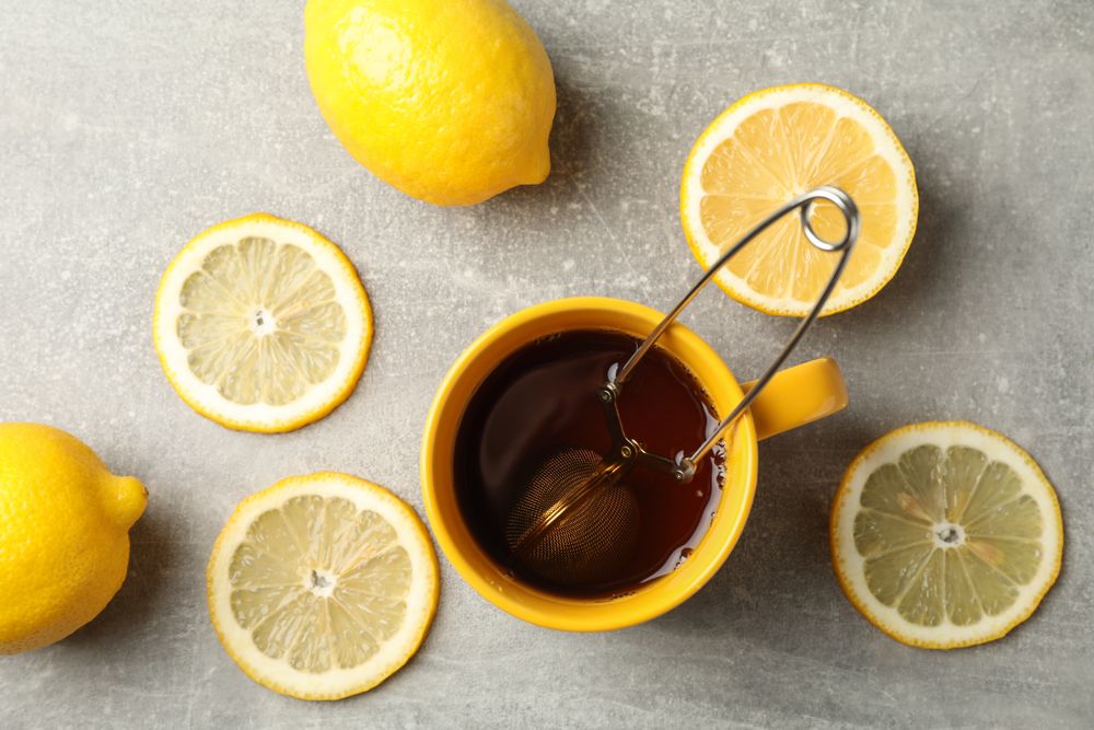 Cup of tea and lemons on grey background, top view