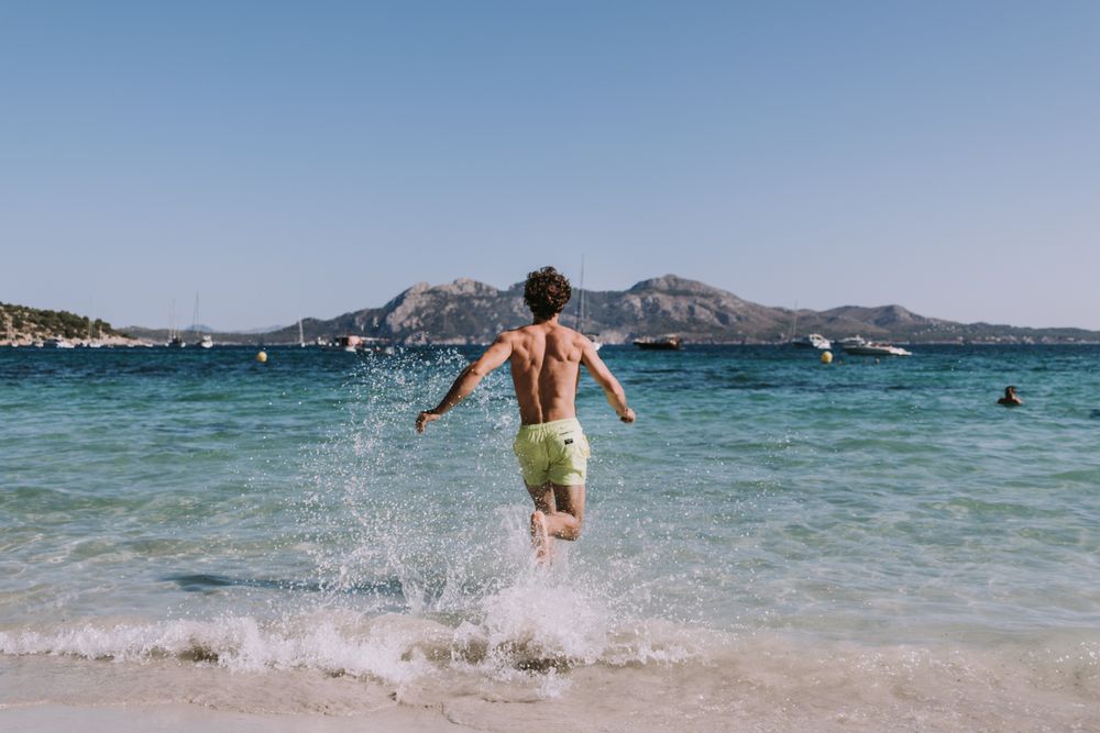 Man in swimsuit running in water on seashore