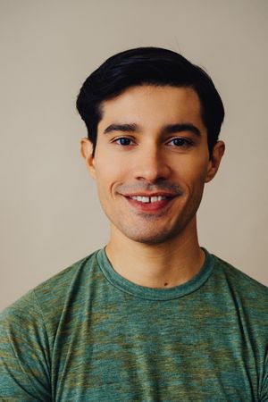 Portrait of smiling Hispanic male in neutral room wearing green t-shirt