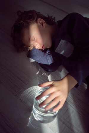 Little kid sleeping on floor with glass jar of water