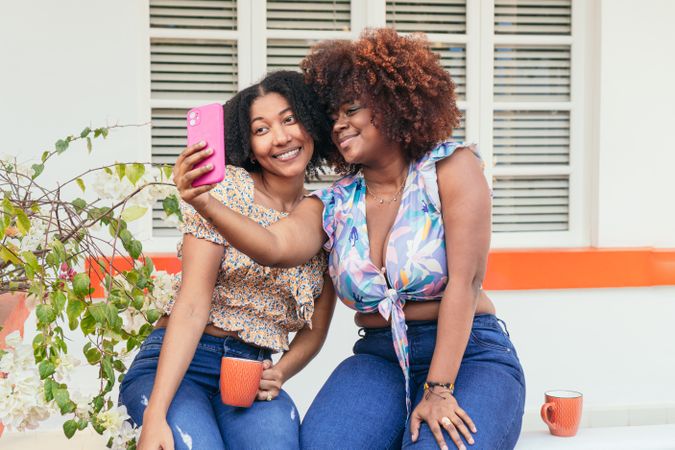 Two Black friends catch up over coffee. They take selfies and chat.