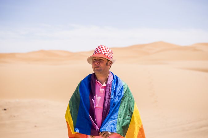 Gay man wrapped in rainbow flag standing in desert