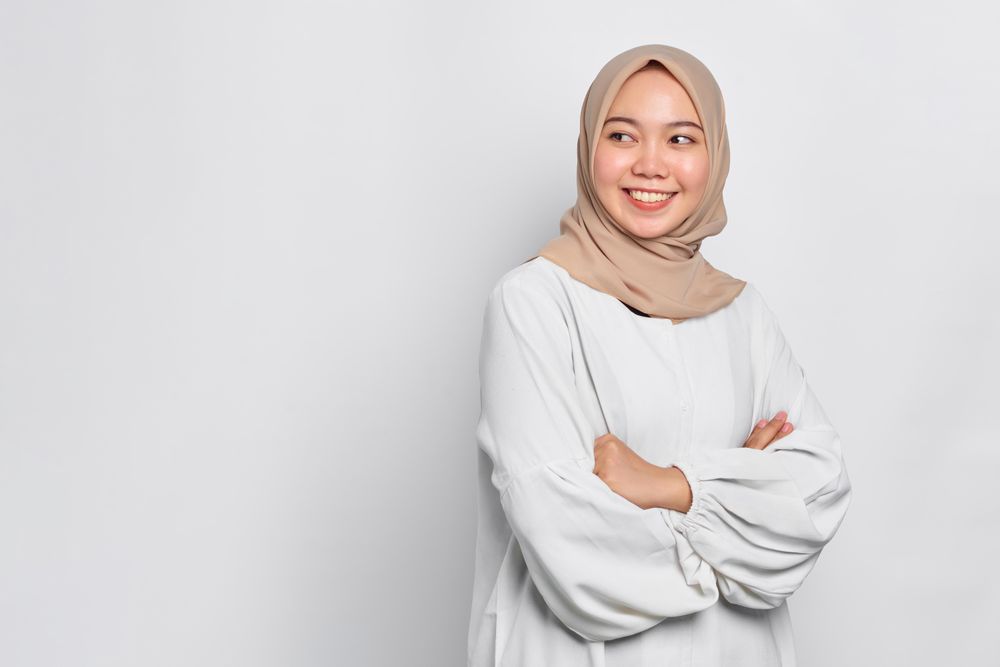 Smiling Asian female in headscarf looking back with arms crossed