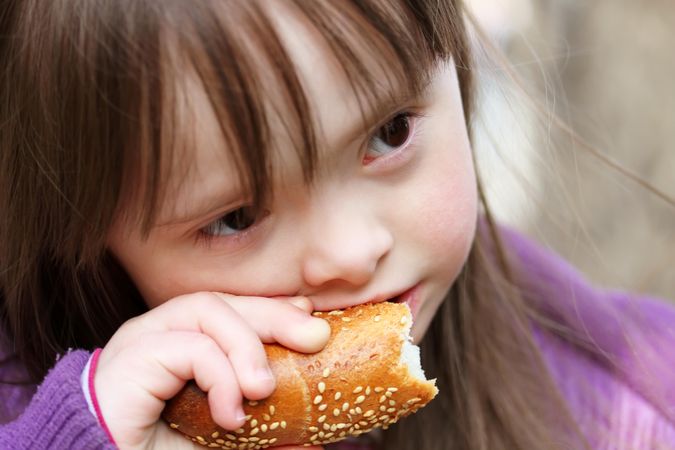 Closeup of a young girl with an intellectual disability biting into a sesame loaf