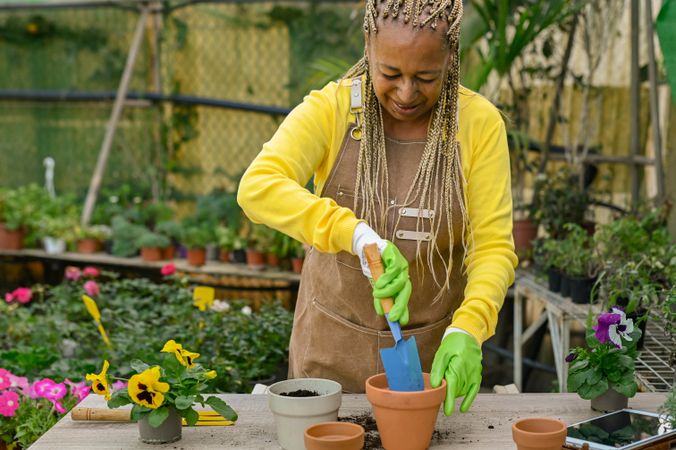 Black woman planting flowers in pots in hothouse