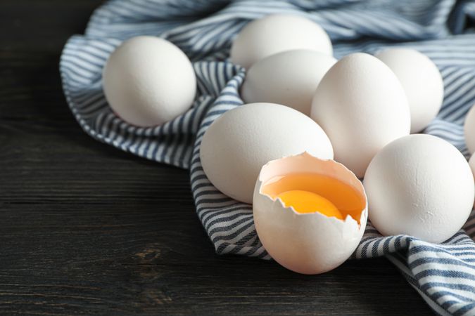 chicken eggs in carton box and kitchen towel on wooden table, space for text and closeup