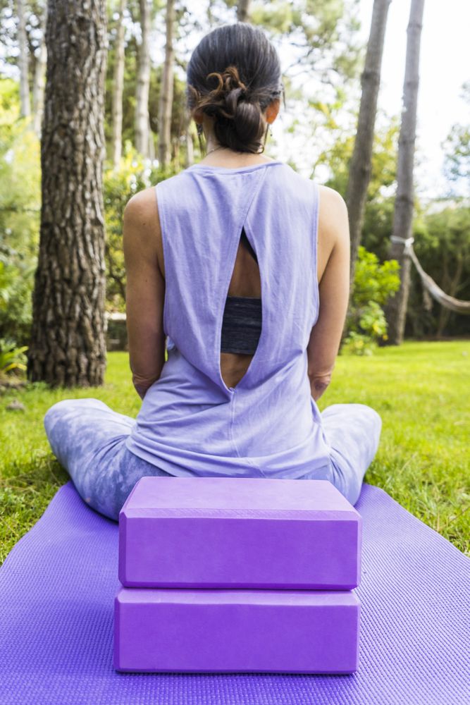 Back view of a woman in sportswear sitting on her yoga mat. Vertical shot