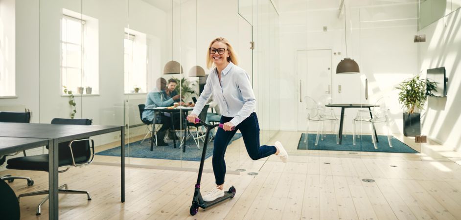Blonde woman riding a scooter in a trendy office