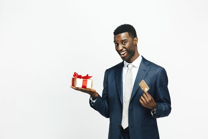 Smiling Black man holding a present wrapped in gold paper and a credit card