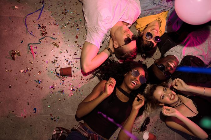 Friends lying on floor at the house party with cups and confetti around