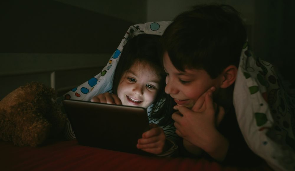 Siblings looking at the tablet in the dark