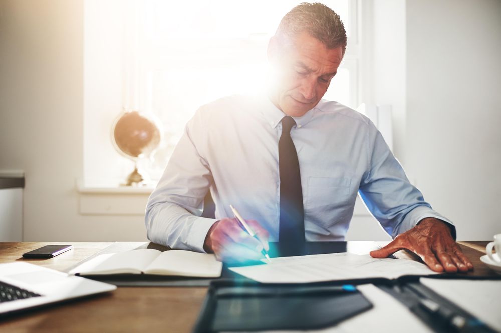 Man in business attire signing documents in his sunny office