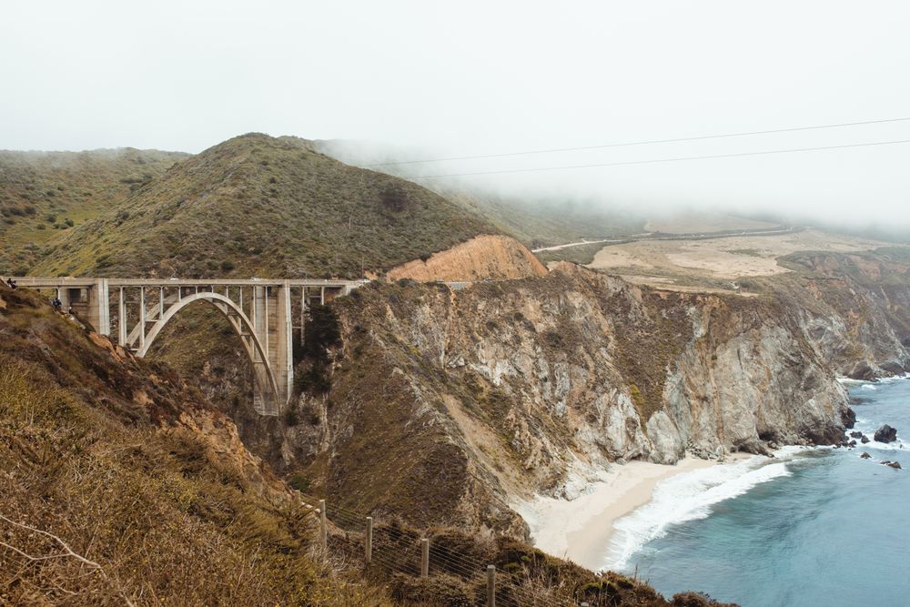 Blue waves washing rocky seashore with bridge in bright day