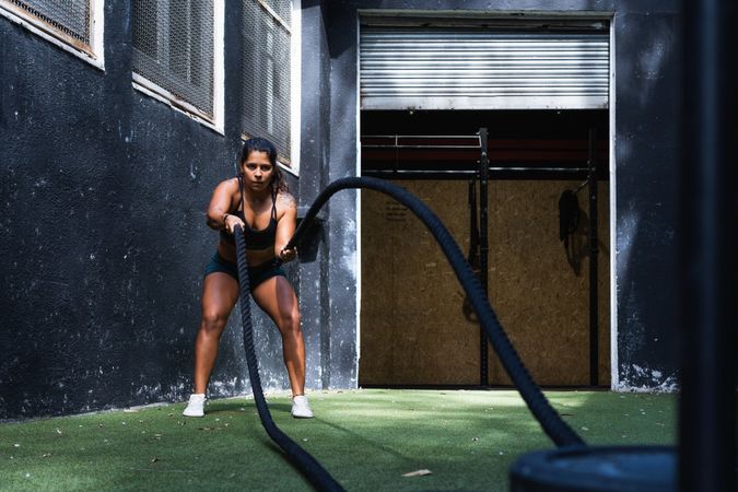 Strong Hispanic woman exercising with battle ropes