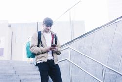 Young man walking down stairs with backpack while using mobile outdoors