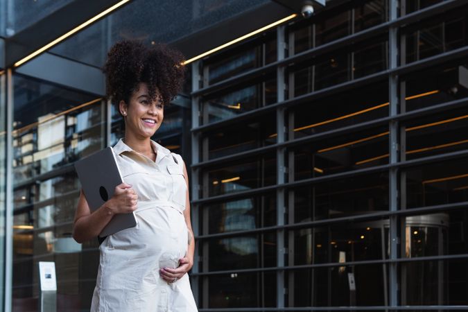 Smiling Black woman with laptop coming out of office building