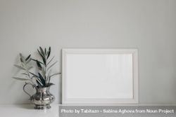 Horizontal wooden picture photo frame on table next to olive twig in vintage silver vase 4A1BY4