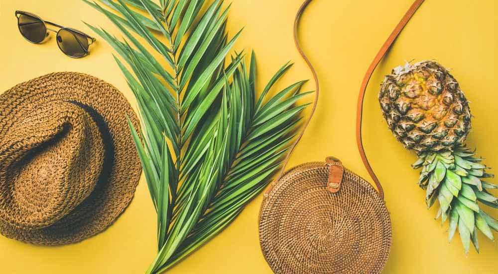 Flat-lay photograph of summery, beach-themed accessories including a hat, purse, sunglasses, a pineapple and palm fronds, linking to a free summer stock photo for commercial use